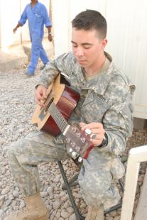 Pfc. Andrew S. Wells, field data tactical system specialist, Bravo Battery, 1st Battalion, 77th Field Artillery Regiment, tunes his guitar at Patrol Base Husayniyah, Iraq, Aug. 22. Wells has to tune his guitar three times every time he plays.  Pfc. Bethany Little